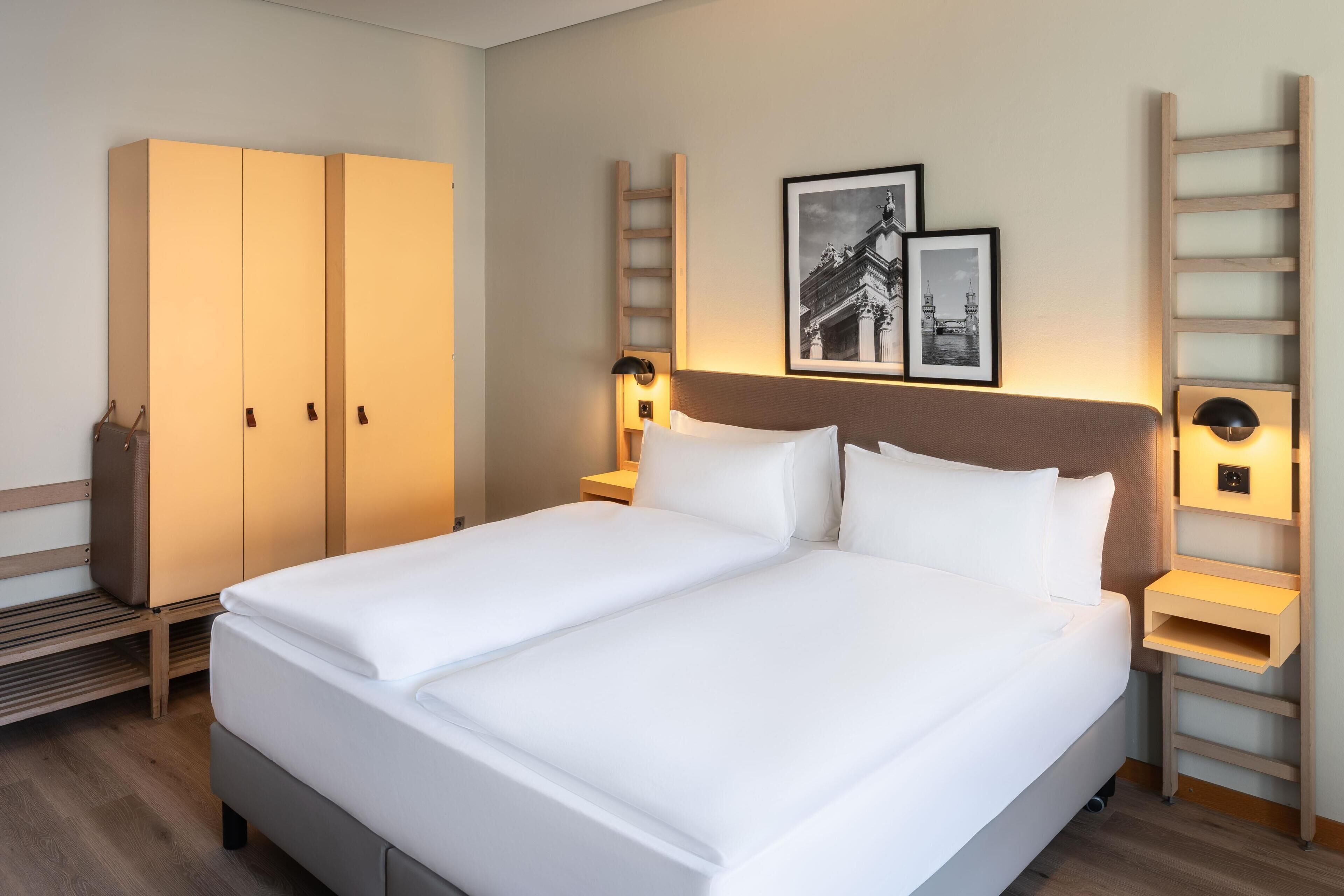 A hotel room with a double bed, a wardrobe, a nightstand, and two wall-mounted lamps.