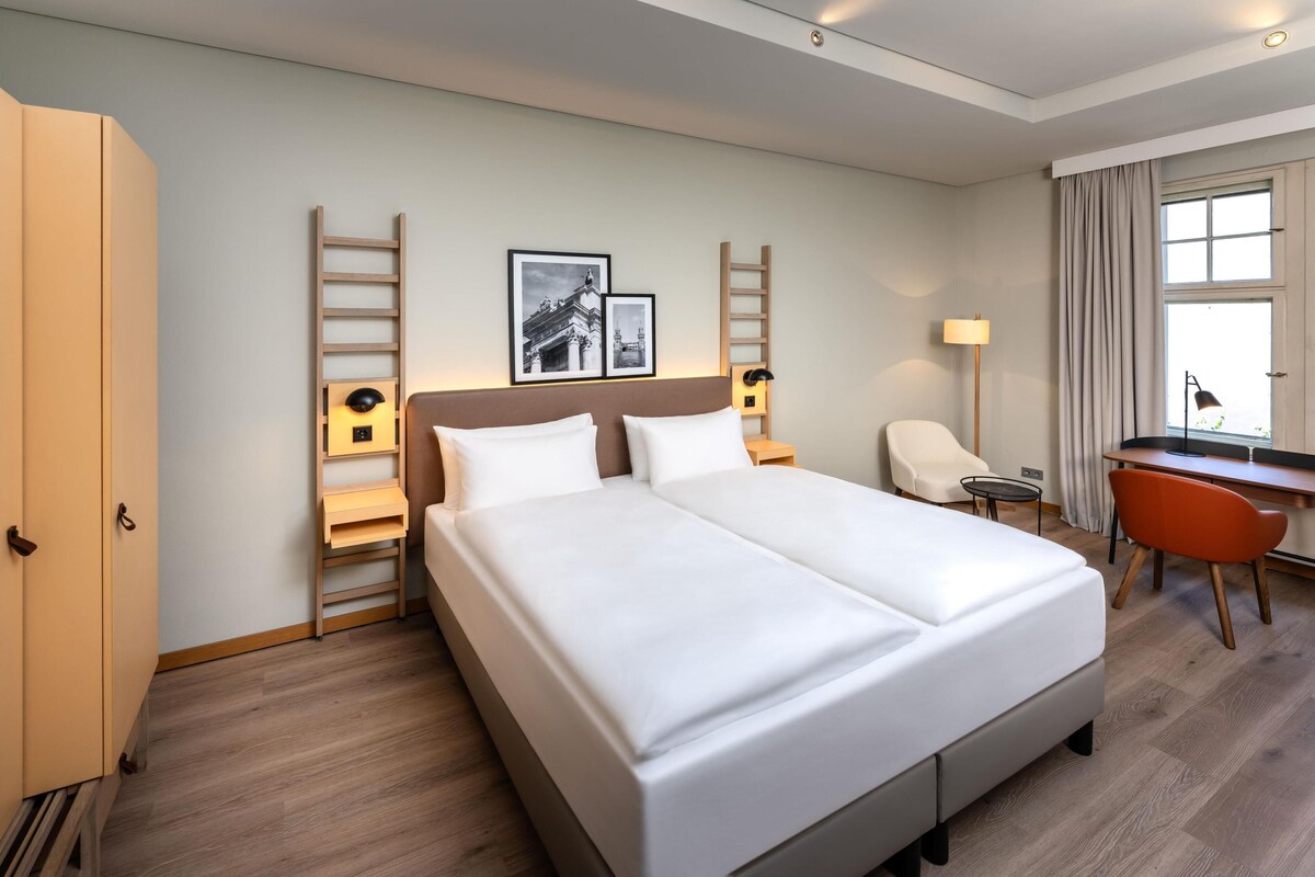 Una habitación de hotel con una cama grande, un escritorio, una silla y dos cuadros en la pared.