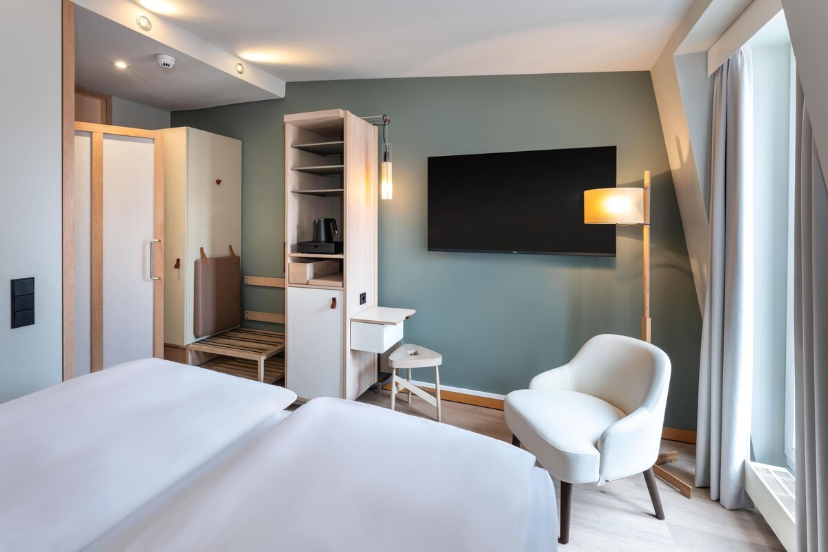 Habitación de hotel con dos camas, un escritorio, una silla, un televisor y un armario.