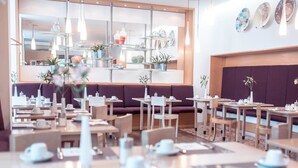 Un café moderno con varias zonas de estar, incluyendo mesas y cabinas, y una variedad de objetos decorativos en estantes.