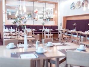 A modern cafe with multiple seating areas, including tables and booths, and a variety of decorative items on shelves. - Hotel Bleibtreu Berlin by Golden Tulip (Berlin)
