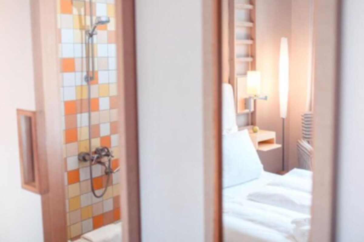 Un baño de hotel con zona de ducha azulejada y una cama con ropa blanca.