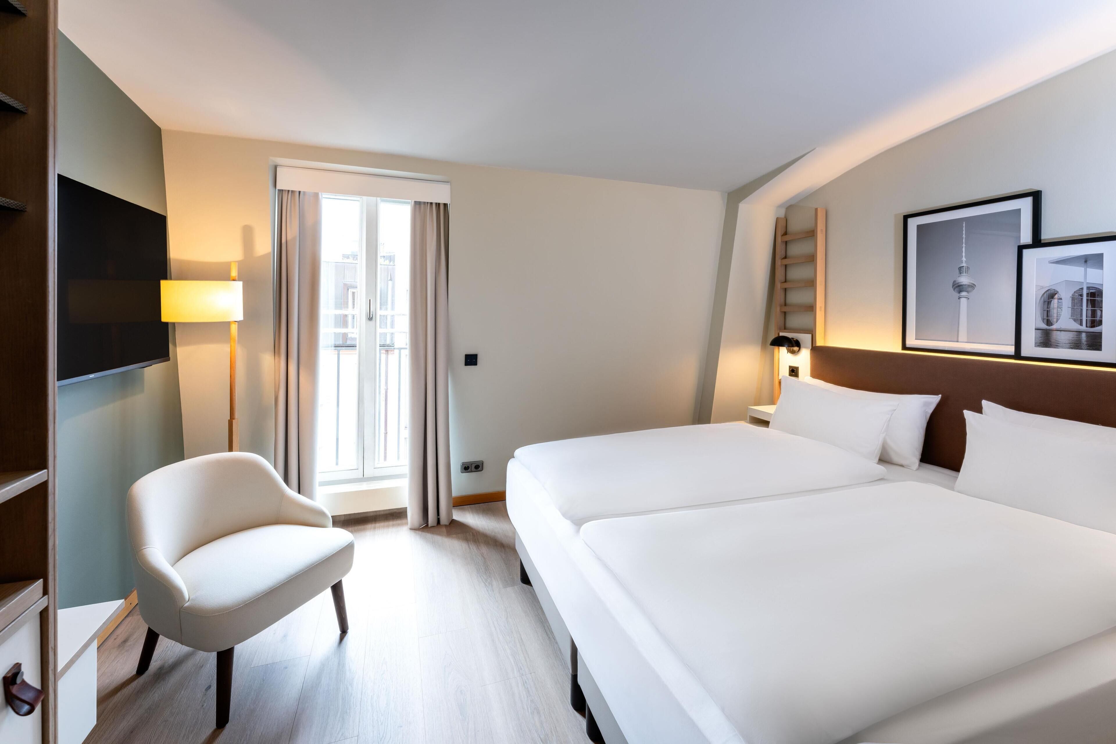 A hotel room with a bed, a chair, a TV, and a window with curtains.