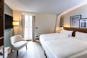 Une chambre d’hôtel avec un lit, une chaise, une télévision et une fenêtre avec des rideaux.