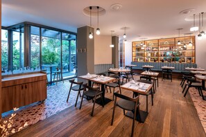 A modern restaurant with large windows, wooden flooring, and a variety of seating arrangements. - Hotel Bleibtreu Berlin by Golden Tulip (Berlin)