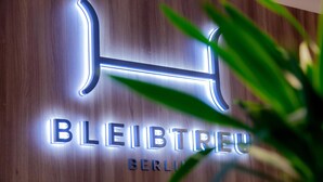 A hotel sign with illuminated letters spelling 'BLEIBTREU BERLIN' on a wooden wall.