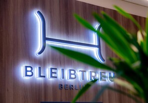 Letrero de hotel con letras iluminadas que dicen 'BLEIBTREU BERLIN' sobre un muro de madera.