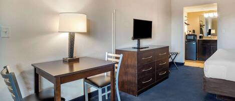 A hotel room with a wooden desk, a chair, a television, a dresser, and a bed.