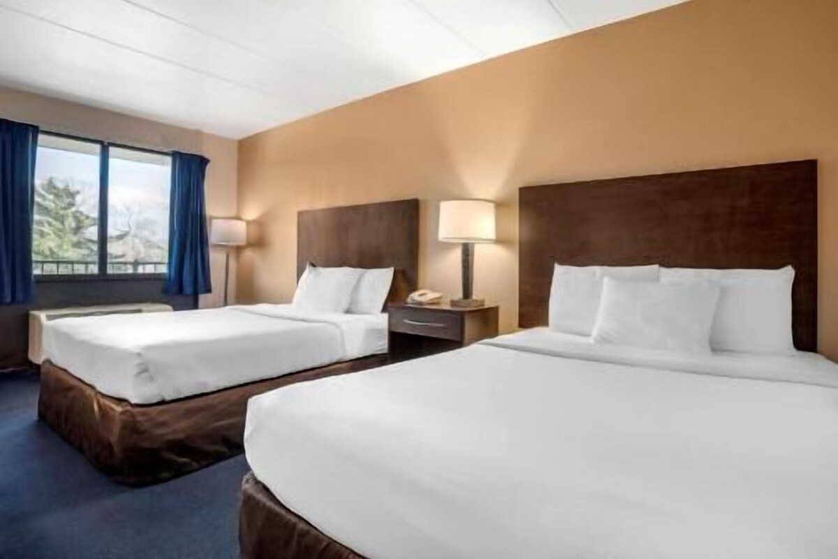 A hotel room with two beds, a nightstand with a lamp, and a window with curtains.