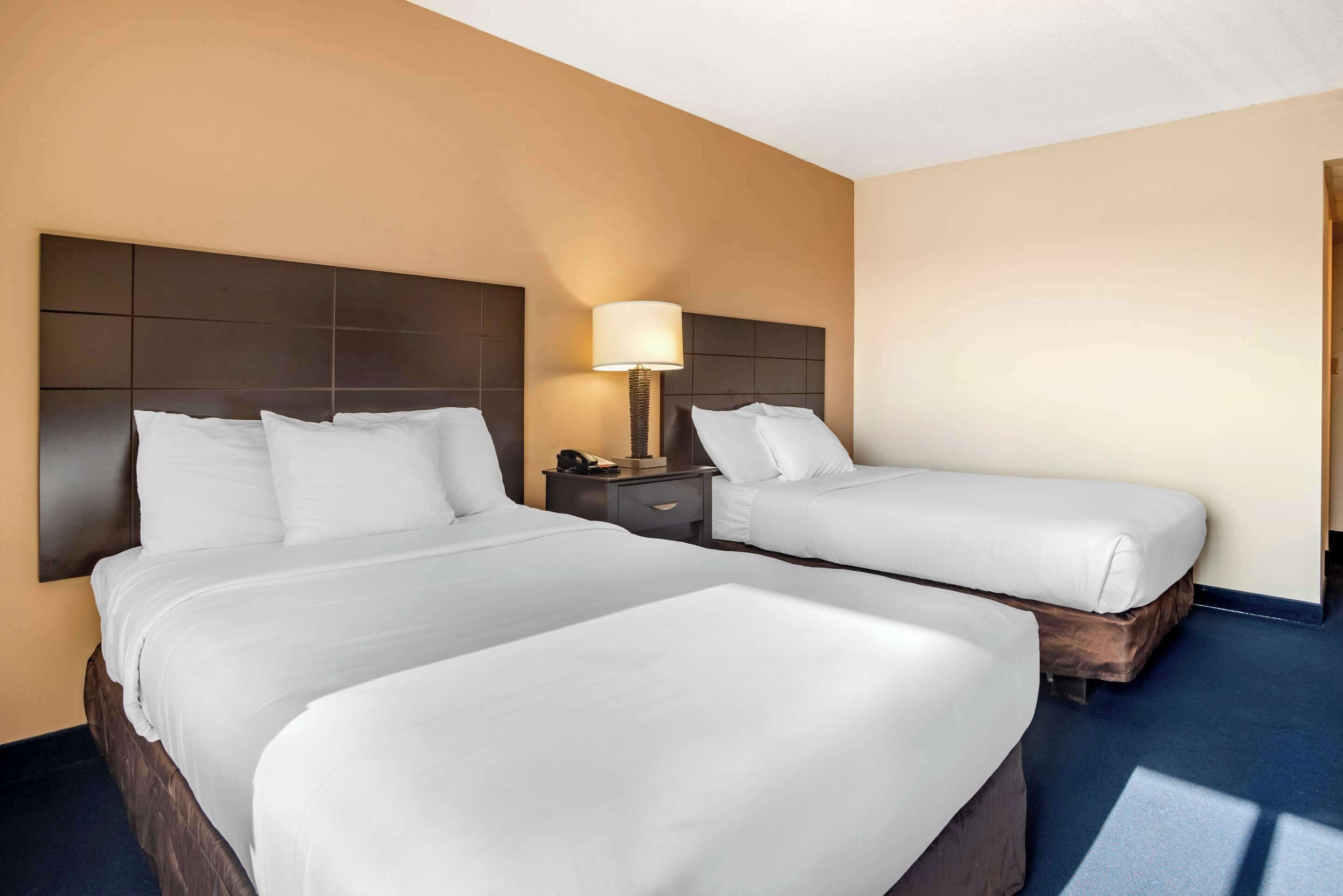 A hotel room with two beds, a nightstand, a lamp, and a wooden headboard.