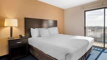 Une chambre d’hôtel avec un grand lit, une table de chevet avec une lampe et une vue sur la ville depuis la porte-fenêtre donnant sur le balcon.