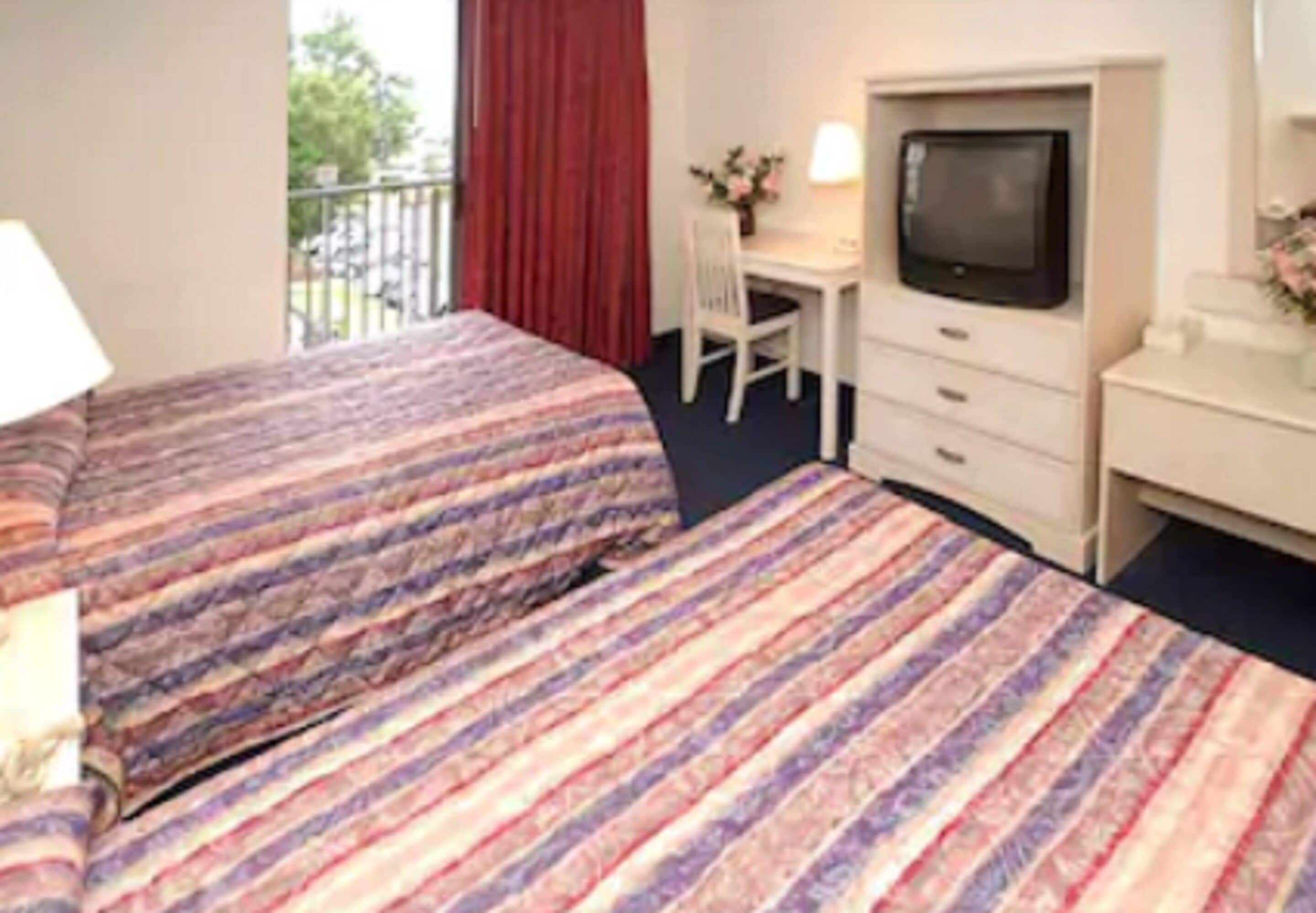 A hotel room with two beds, a desk, a chair, a TV, and a window with a view of the outside.