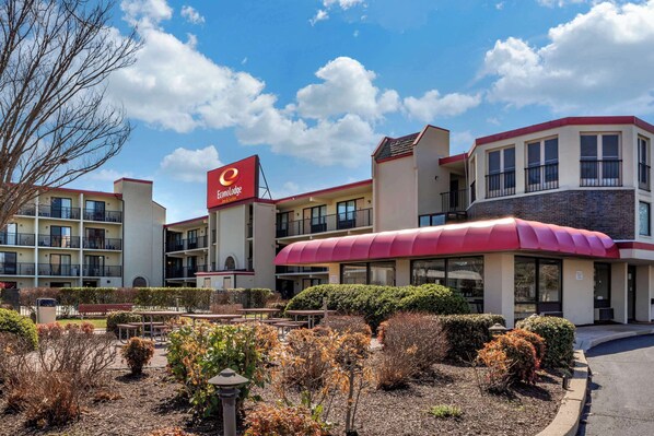A hotel with a red awning, multiple balconies, and a landscaped courtyard with benches and shrubs.