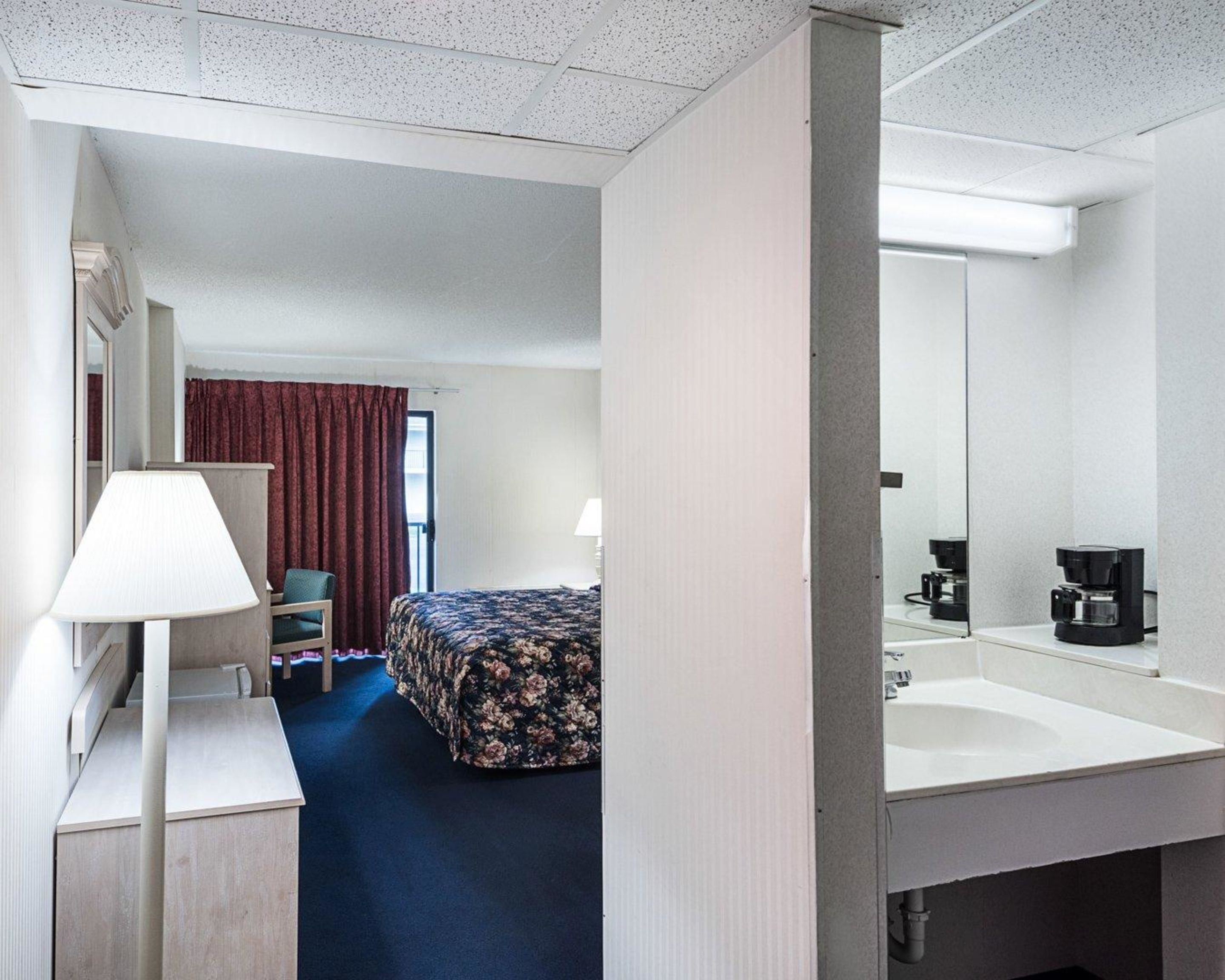 Habitación de hotel con cama, escritorio, silla, lámpara, cafetera y espejo.