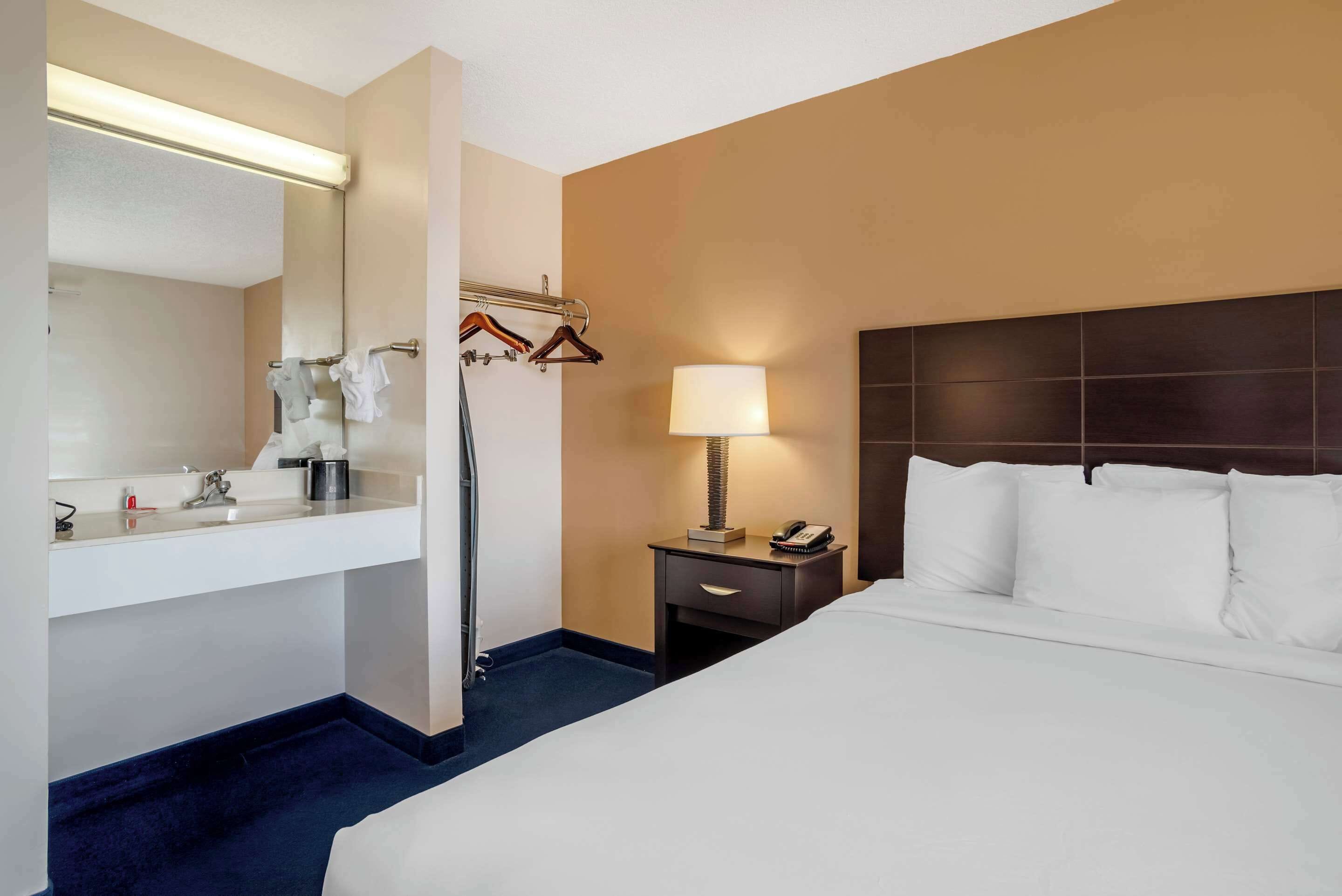 Une chambre d’hôtel avec un grand lit, une table de chevet avec une lampe, un miroir, un lavabo et un porte-serviettes.