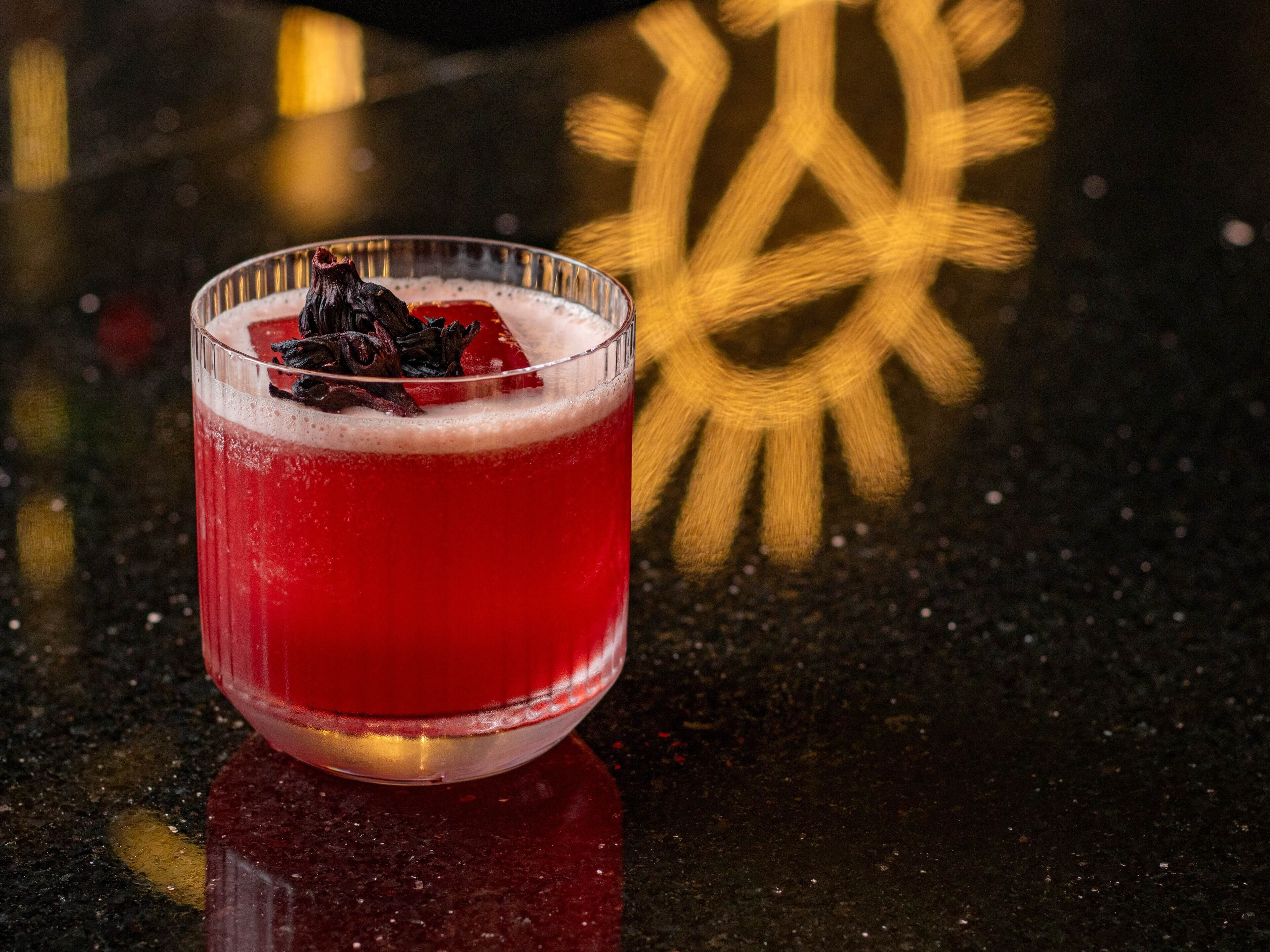 A glass of red beverage with a garnish on a reflective surface.