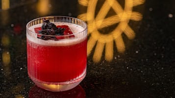 A glass of red beverage with a garnish on a reflective surface.