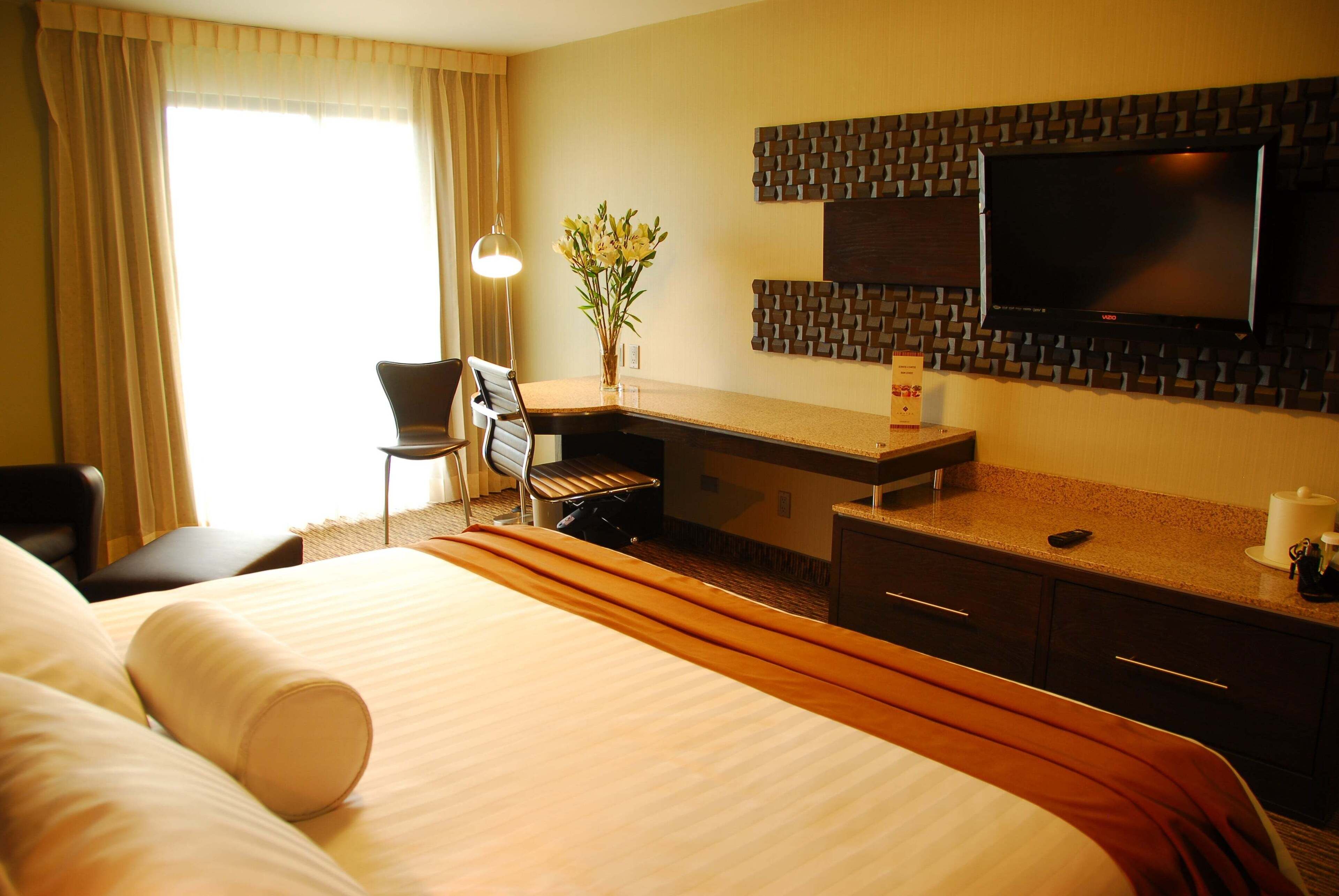 Una habitación de hotel con cama, escritorio, silla, televisión y un florero con flores.
