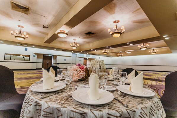 Salão de banquetes com mesas redondas preparadas para refeições, com pratos brancos, guardanapos e copos.