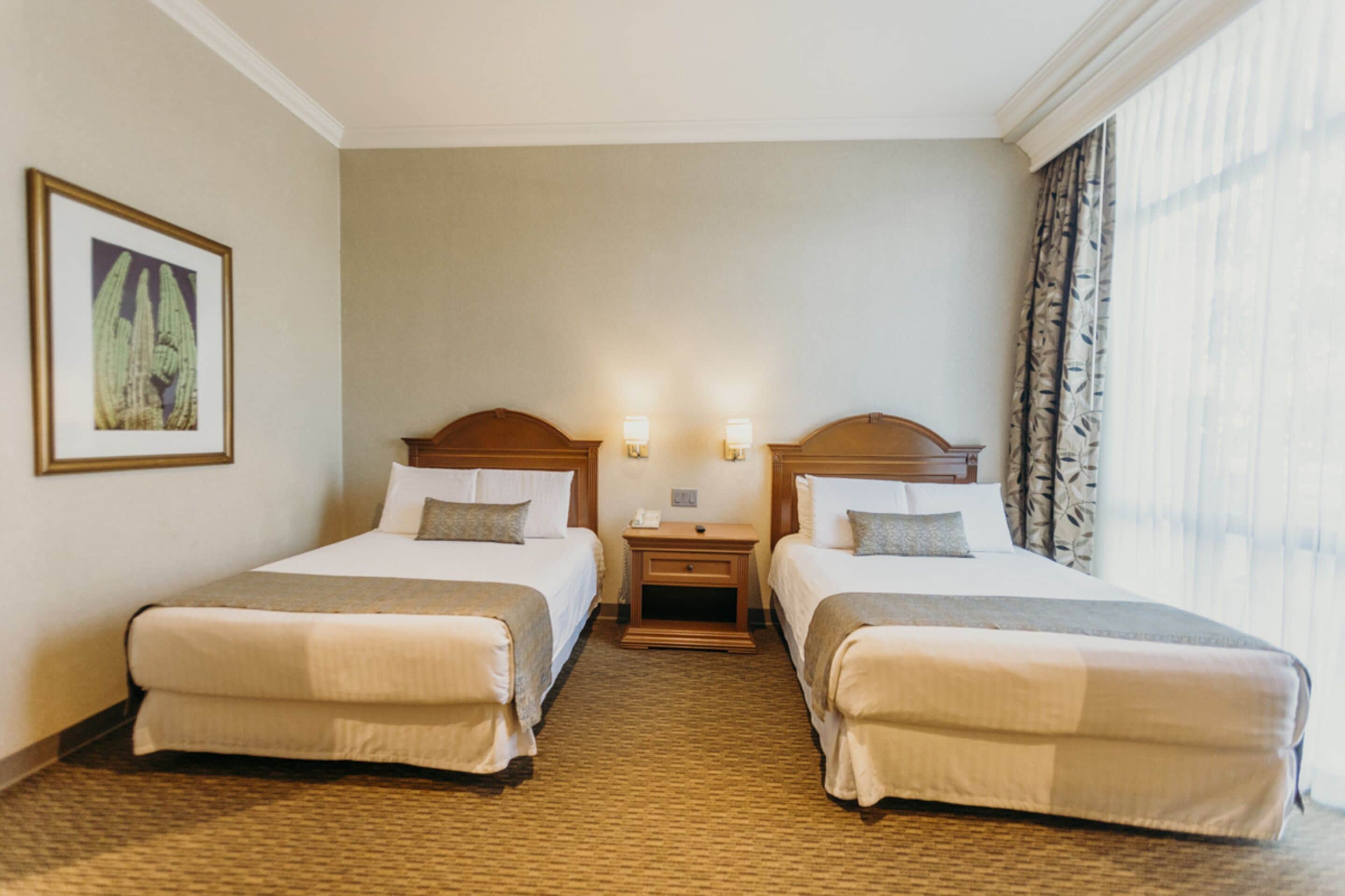 A hotel room with two beds, a nightstand, and a framed picture on the wall.