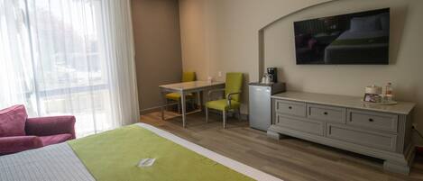 Habitación de hotel con cama, escritorio, silla, refrigerador pequeño y televisión de pantalla plana montada en la pared.