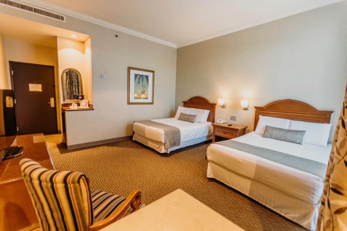 A hotel room with two beds, a chair, a desk, and a mirror.