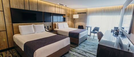 Habitación de hotel con dos camas, un escritorio, una silla, un televisor y un ventanal con cortinas.