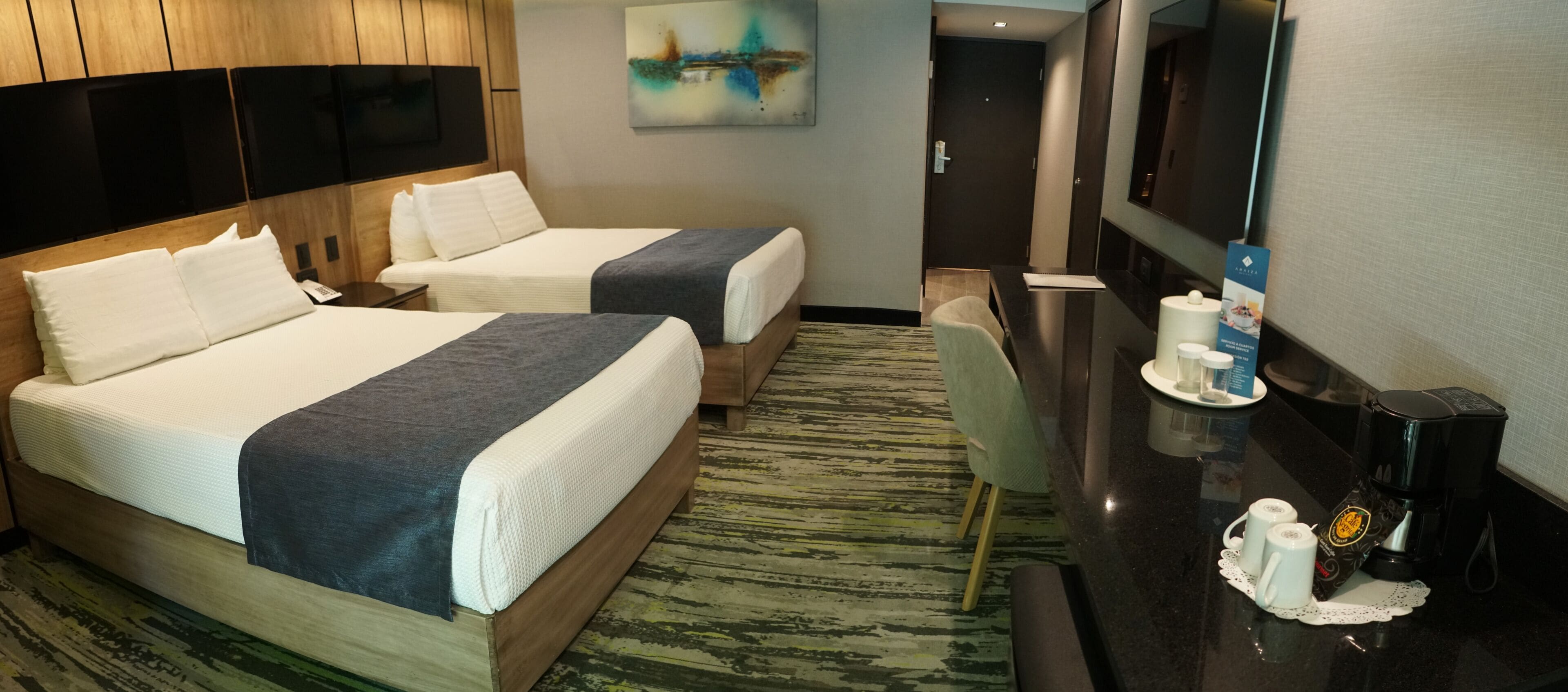 A hotel room with two beds, a desk with a coffee maker, and a television.