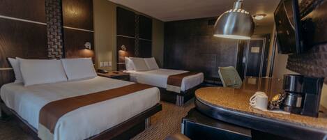 A hotel room with two beds, a desk with a coffee maker, a mirror, and a TV mounted on the wall.
