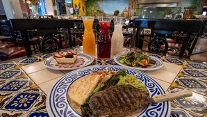 A dining table with a variety of dishes including a steak, salad, and a dessert. There are also two drinks on the table. - Hotel Araiza Mexicali (Mexicali)