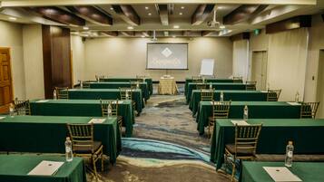 Une salle de conférence avec des tables et des chaises vertes, un sol recouvert de moquette et un écran affichant le logo de « Bonquêts Catering ».