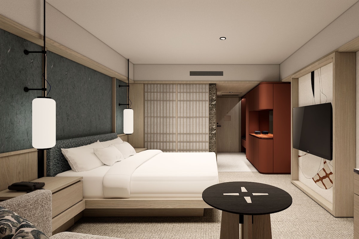 Een moderne hotelkamer met een bed, nachtkastje, televisie en een klein rond tafeltje.