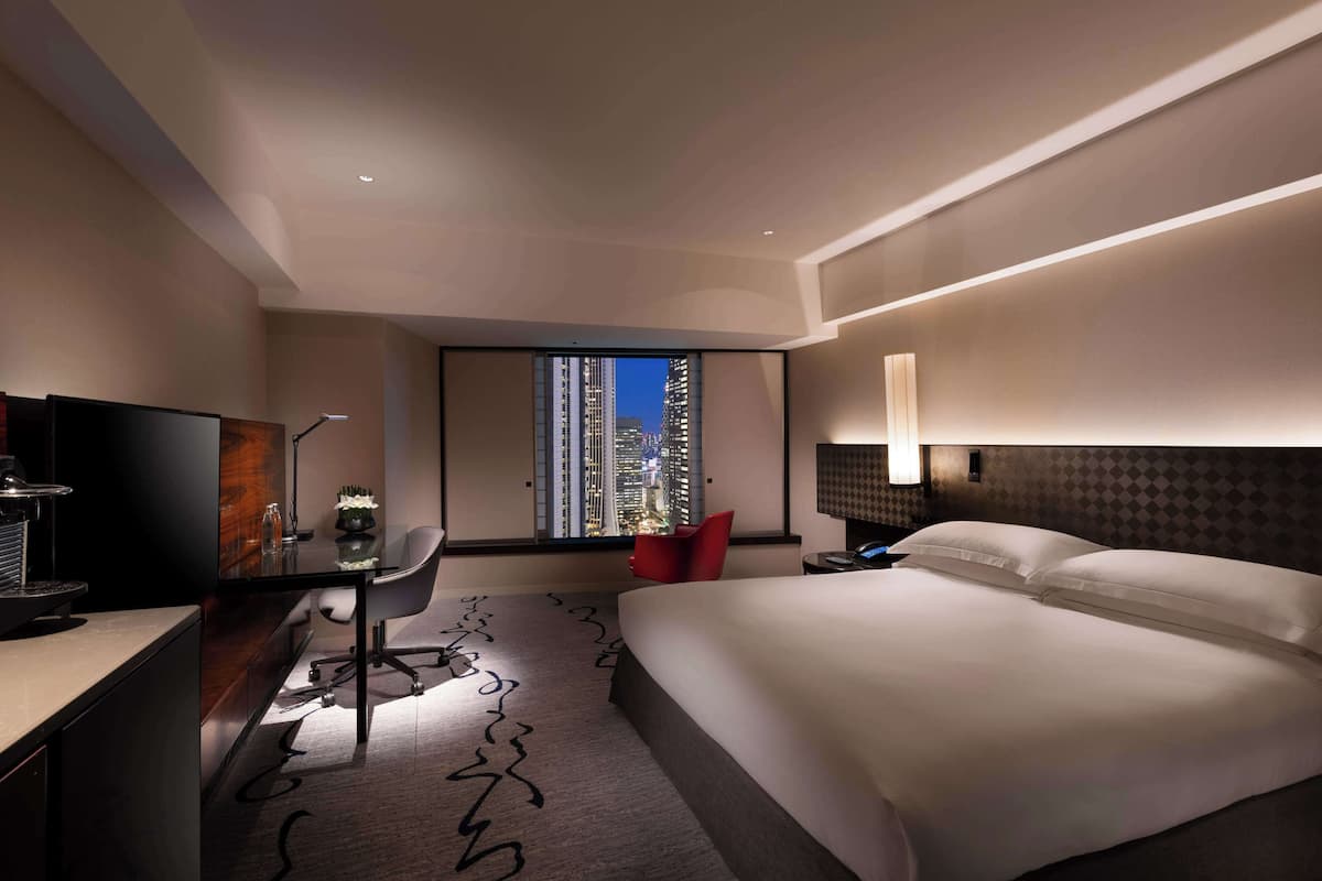 A modern hotel room with a large bed, a desk with a chair, a television, and a window with a city view.