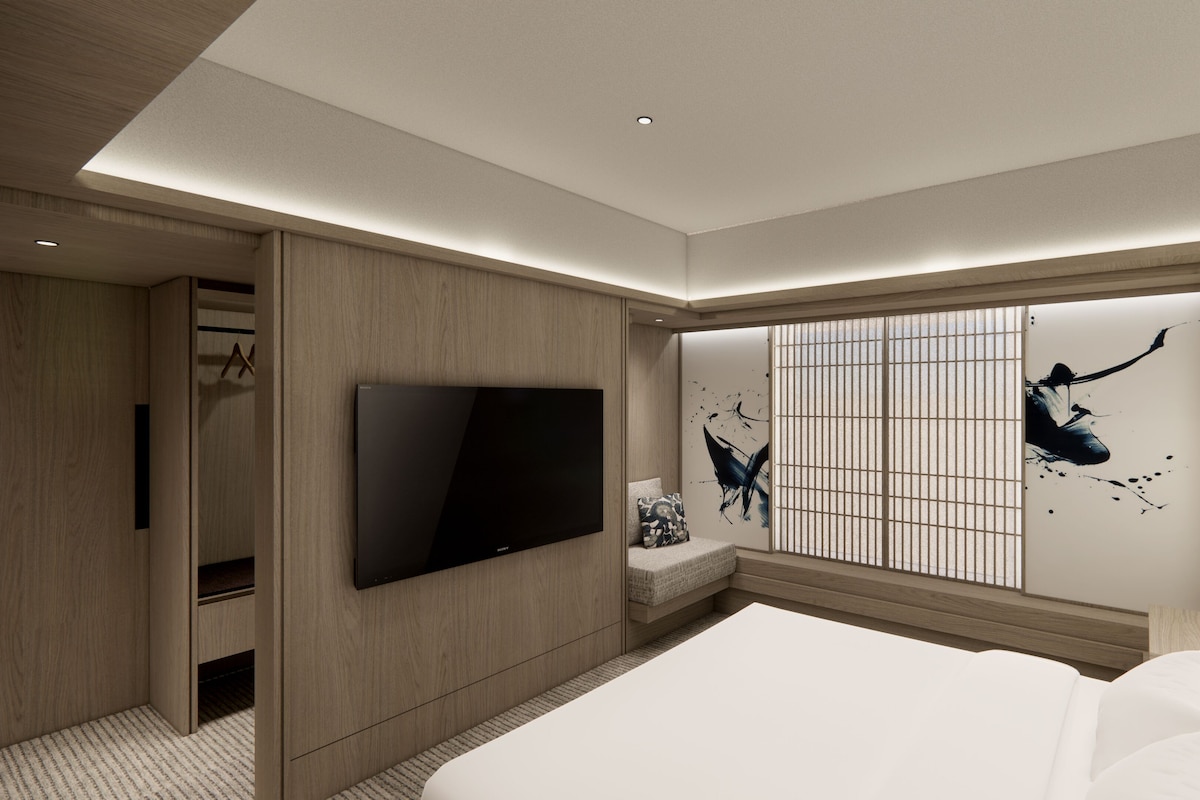 Een moderne hotelkamer met een groot bed, een flatscreen-televisie aan de muur, een zithoek met een comfortabele bank en een decoratieve wand met abstracte kunst.