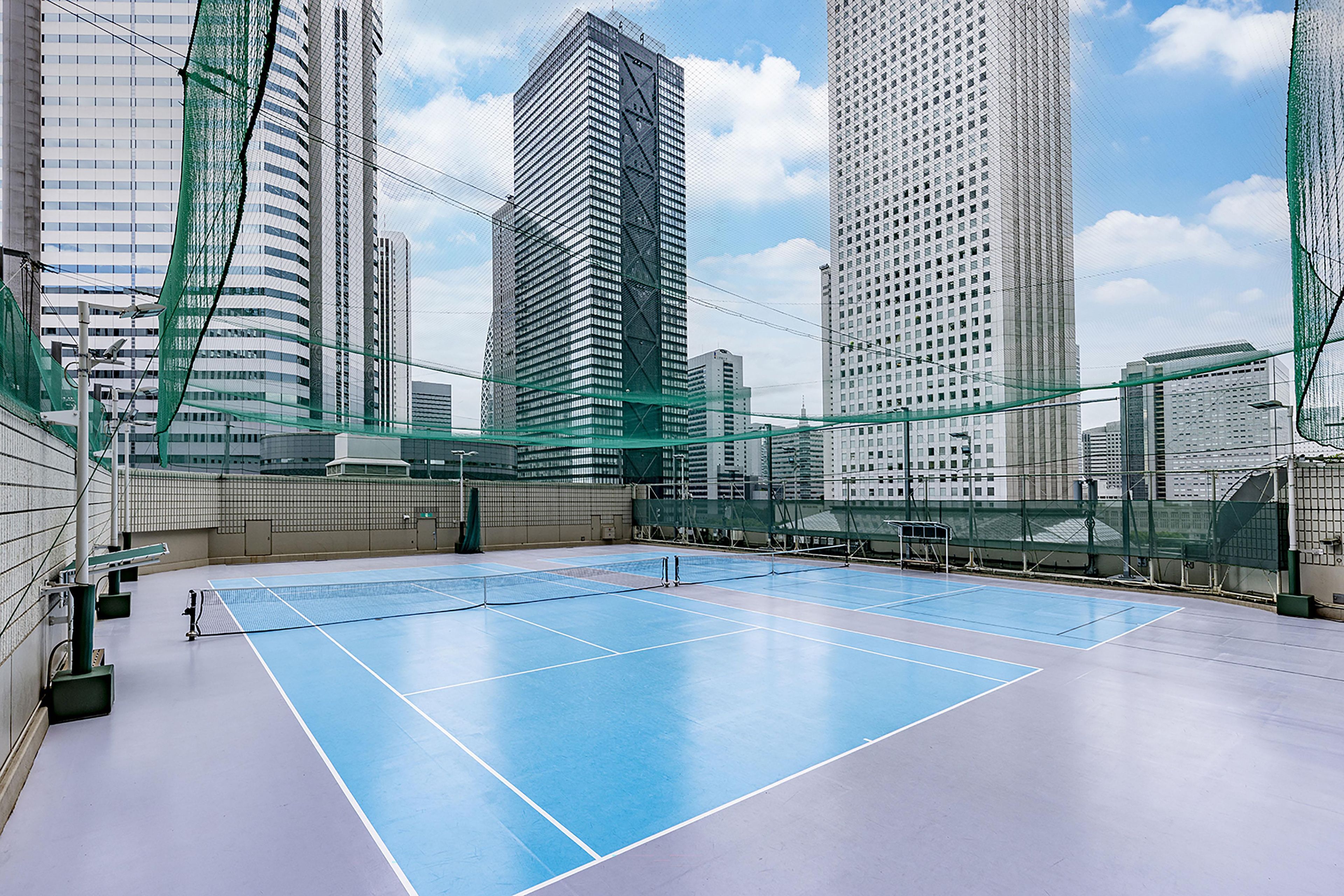 Ein Tennisplatz im Freien, umgeben von Hochhäusern.