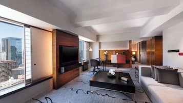 Habitación de hotel moderna con televisor grande, sofá, mesa de centro y vista panorámica de la ciudad.