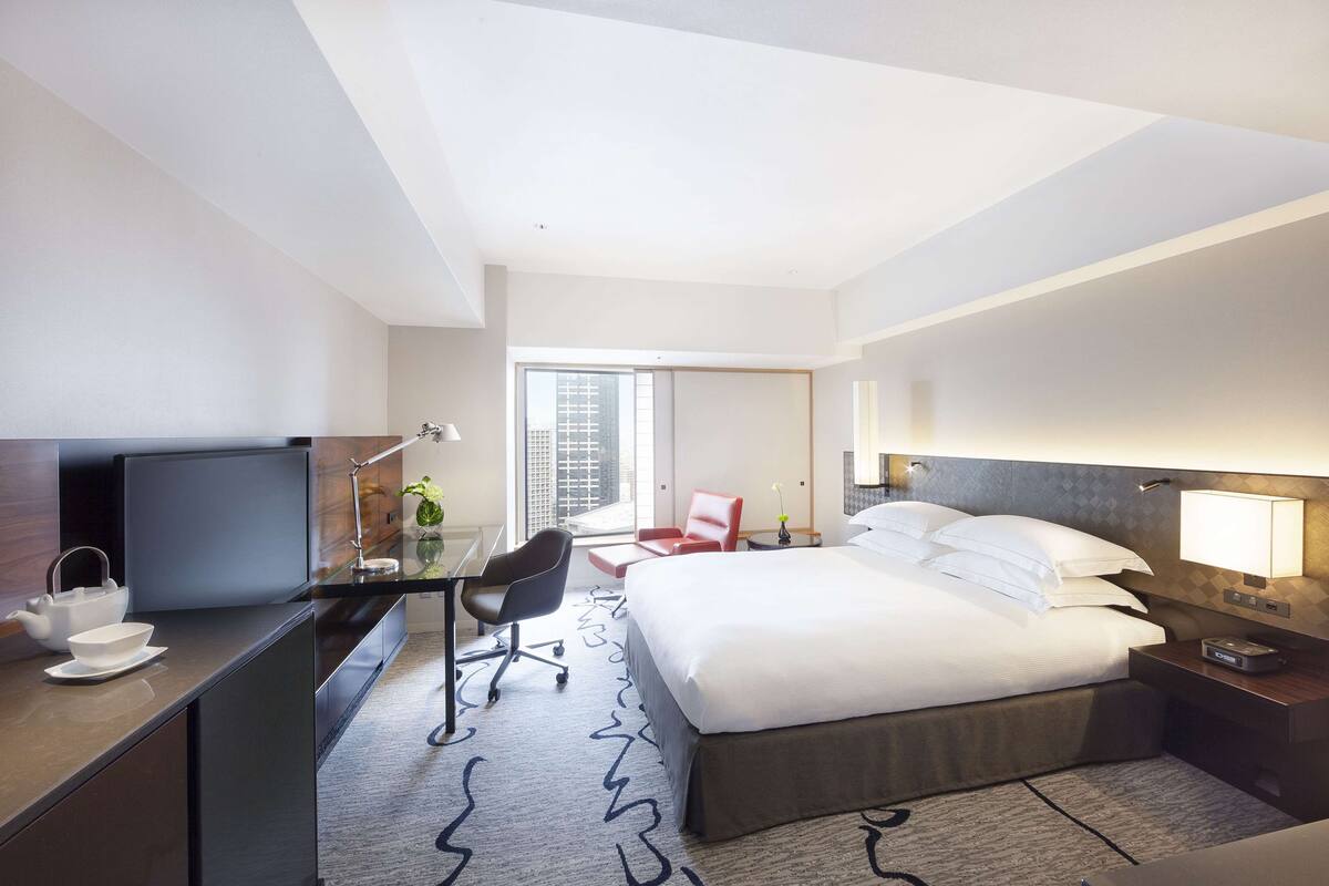 A modern hotel room with a large bed, a desk with a computer, a chair, and a TV.