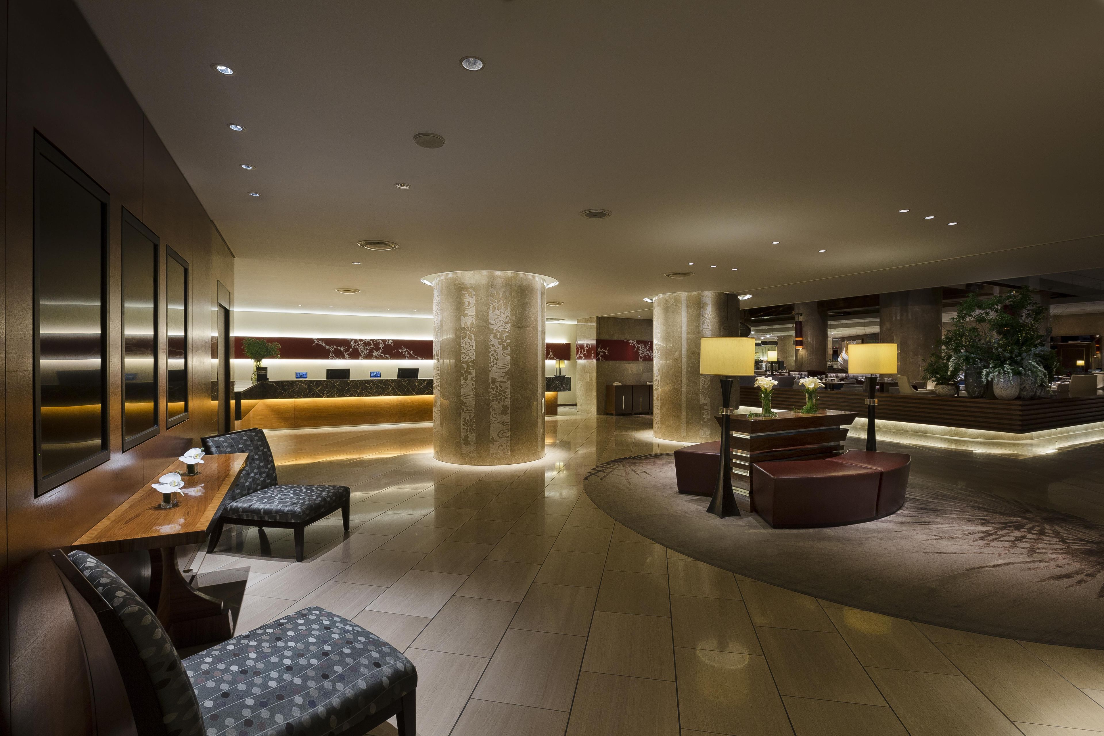 A modern hotel lobby with a reception desk, seating area, and decorative columns.
