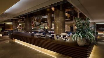 Eine großzügige Lobby mit einer zentralen Rezeption, mehreren Sitzbereichen und einer großen Zimmerpflanze.