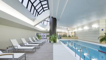An indoor swimming pool with lounge chairs and a high ceiling with skylights.