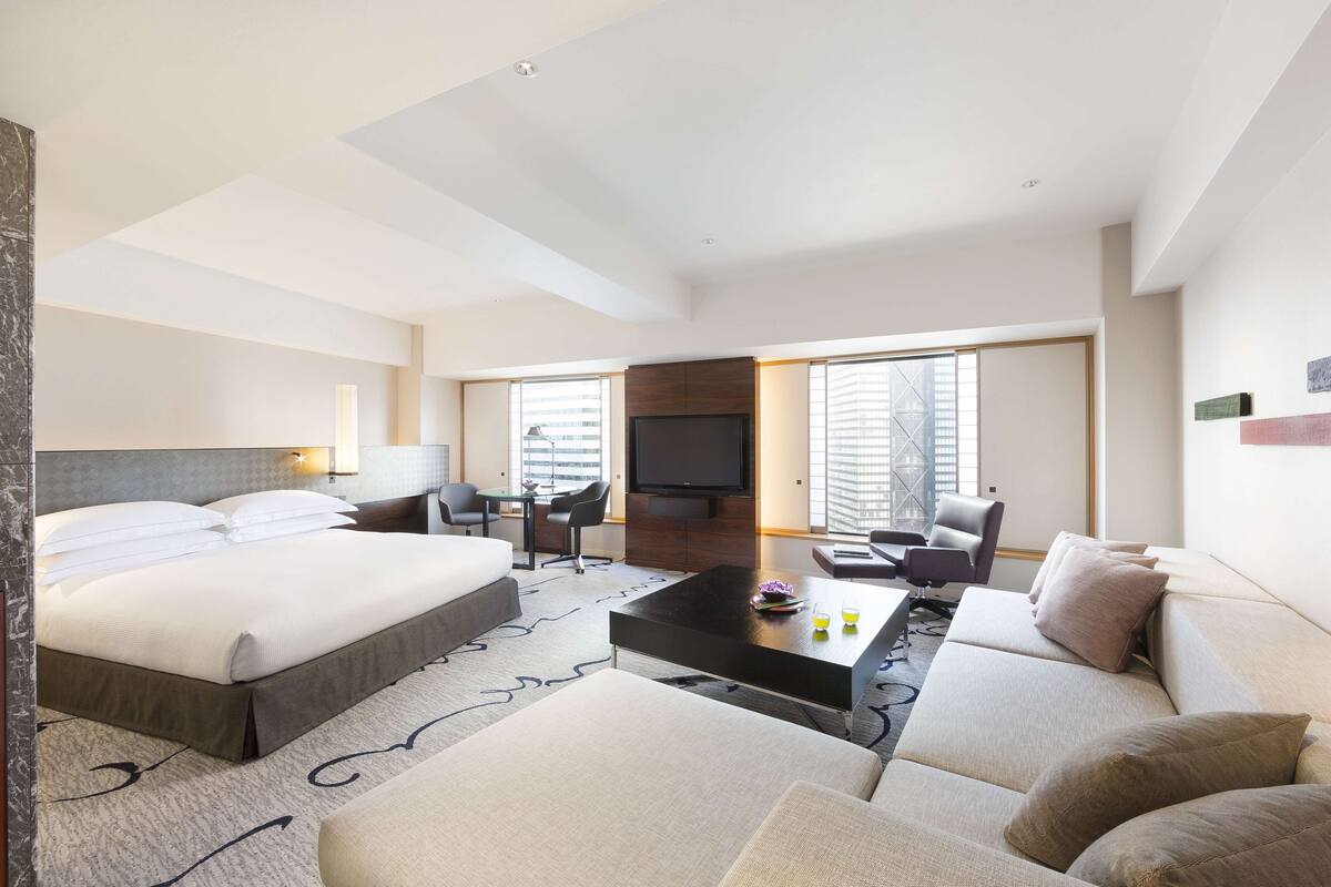 A modern hotel room with a large bed, a sofa, a coffee table, and a TV.