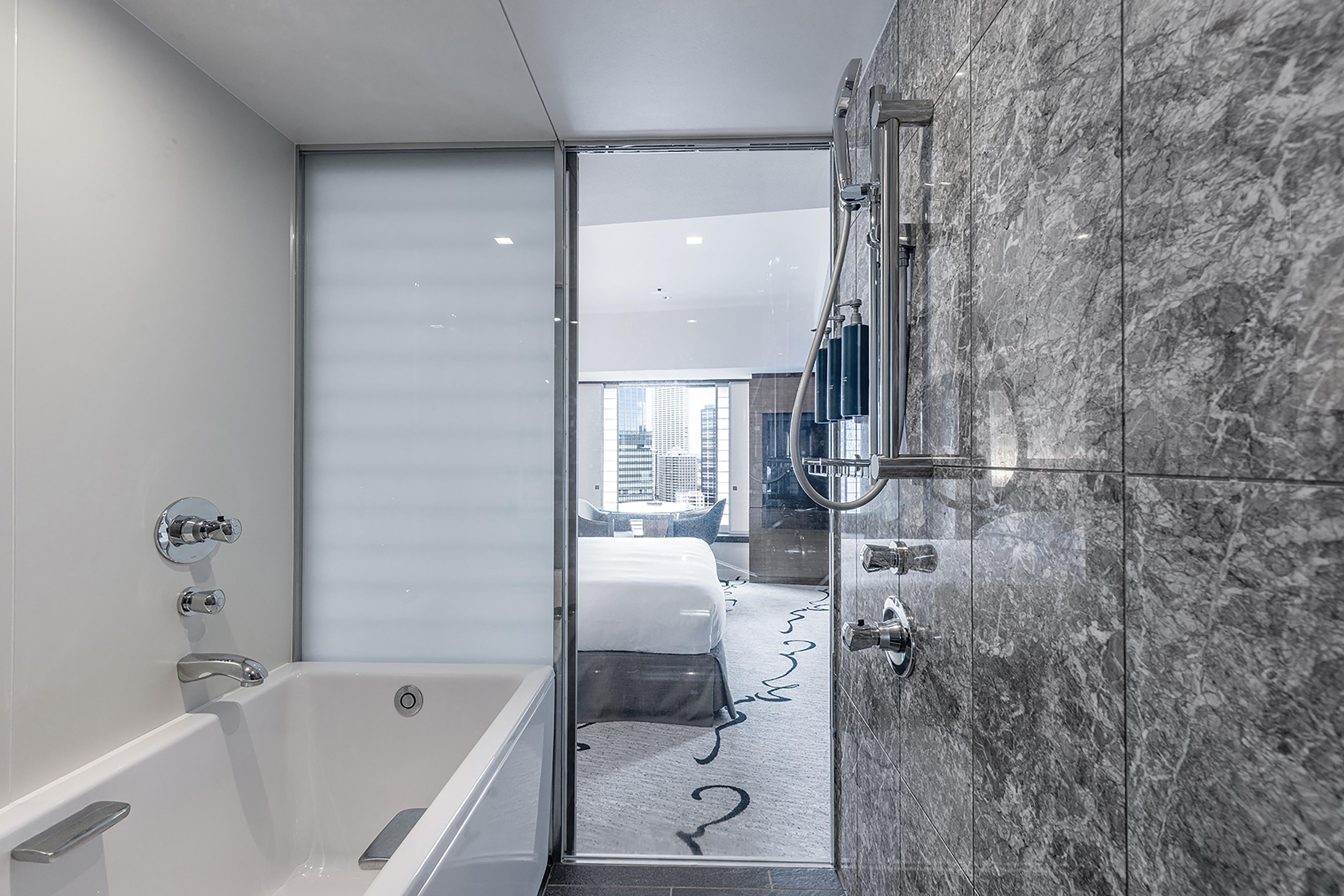 A modern bathroom with a bathtub, shower, and marble walls.