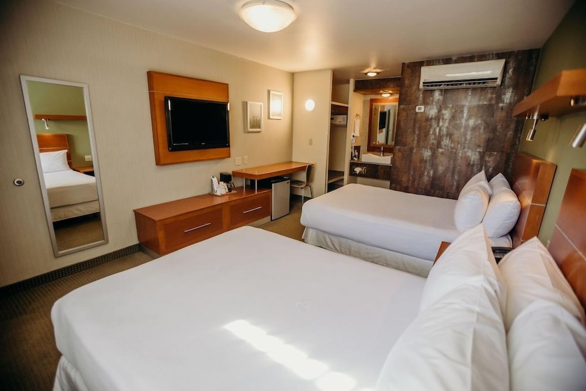 A hotel room with two beds, a desk, a mirror, and an air conditioning unit.