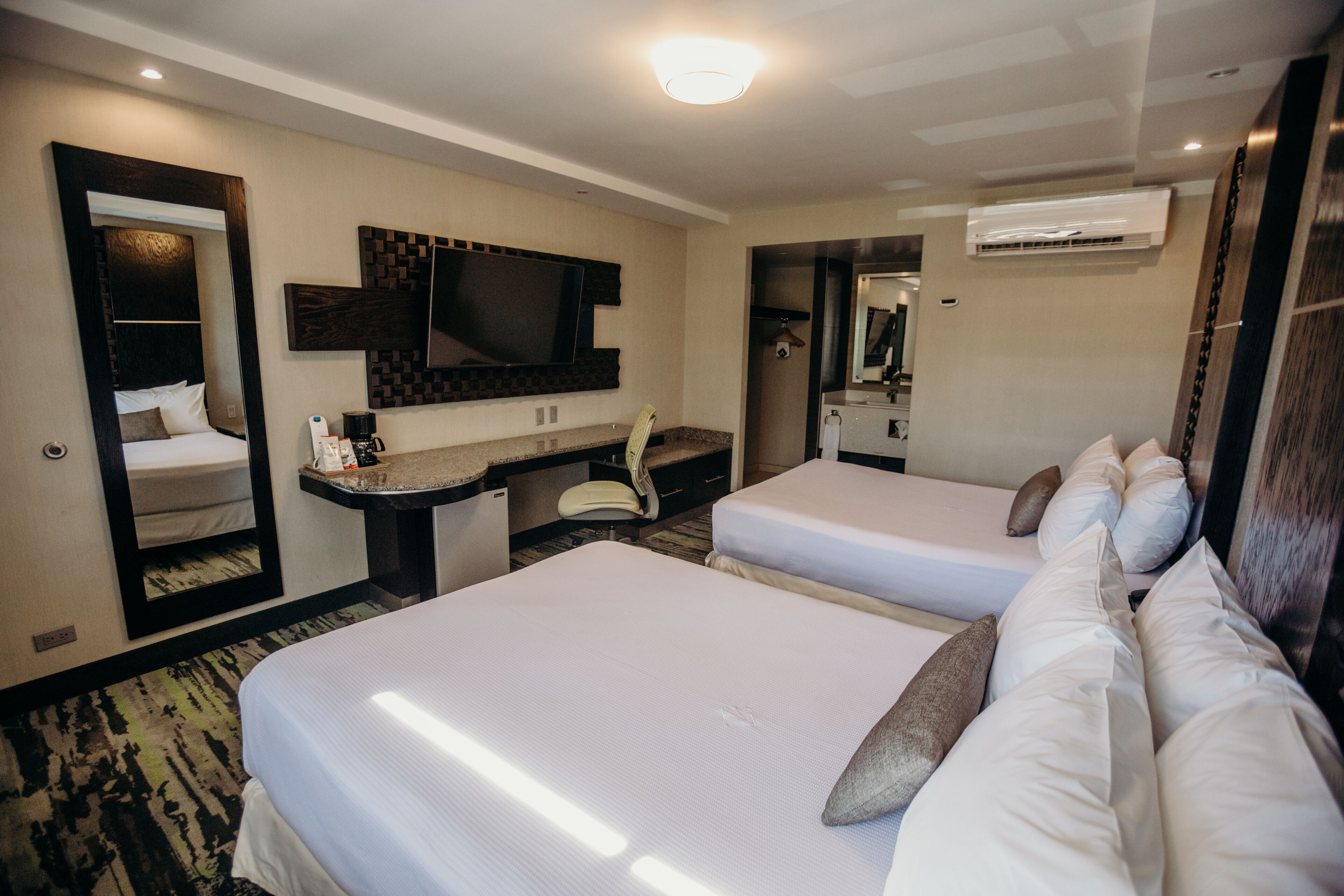 Une chambre d’hôtel avec deux lits, un bureau, une chaise, une télévision et un appareil de climatisation.