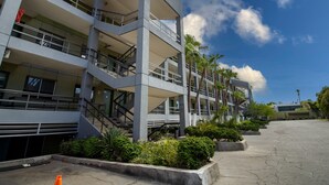 A multi-story building with balconies, a parking area, and palm trees.