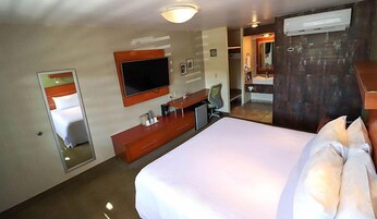 A hotel room with a bed, a desk, a chair, a TV, and a mirror.