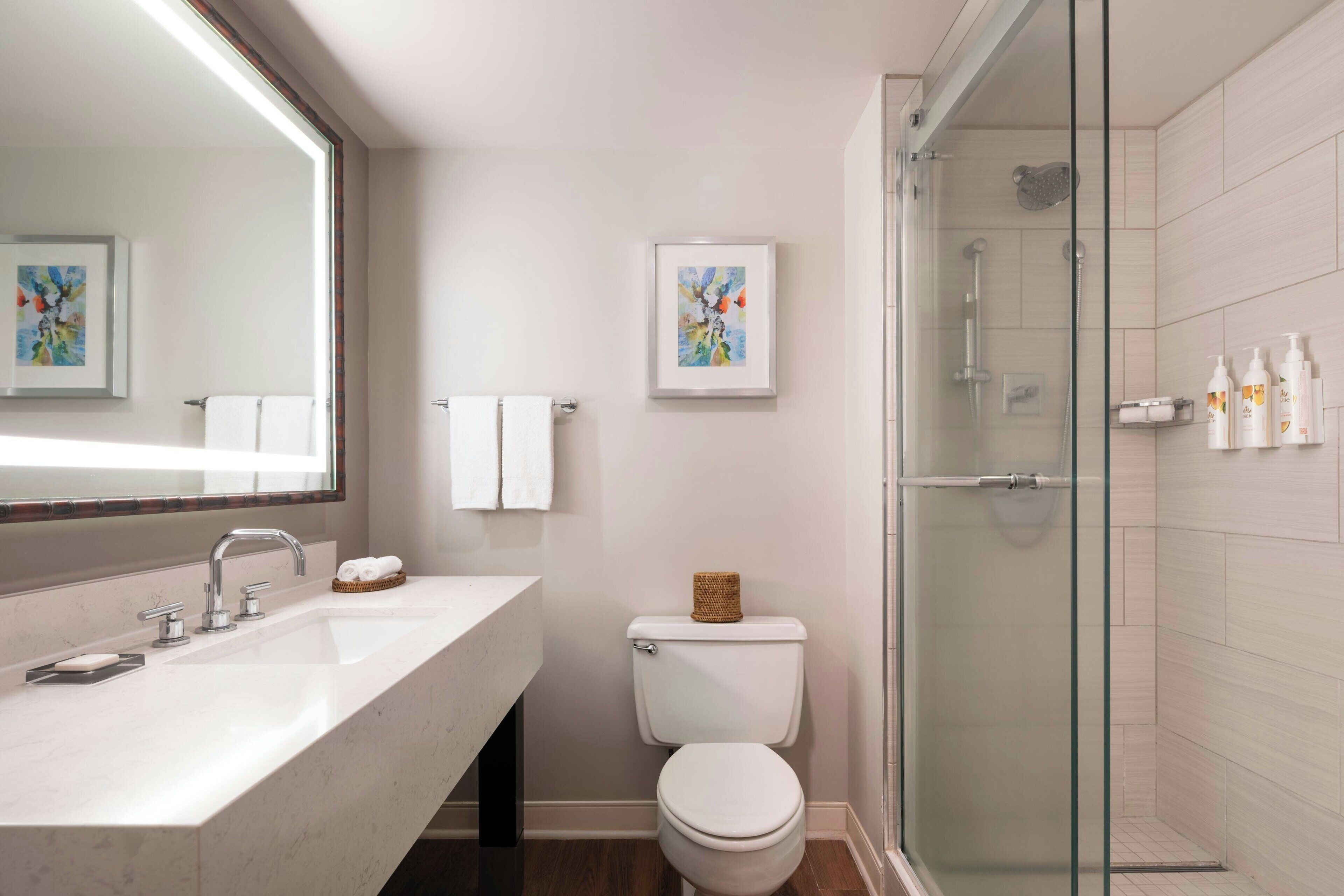 A modern bathroom with a large mirror, a white sink, a toilet, and a glass-enclosed shower.