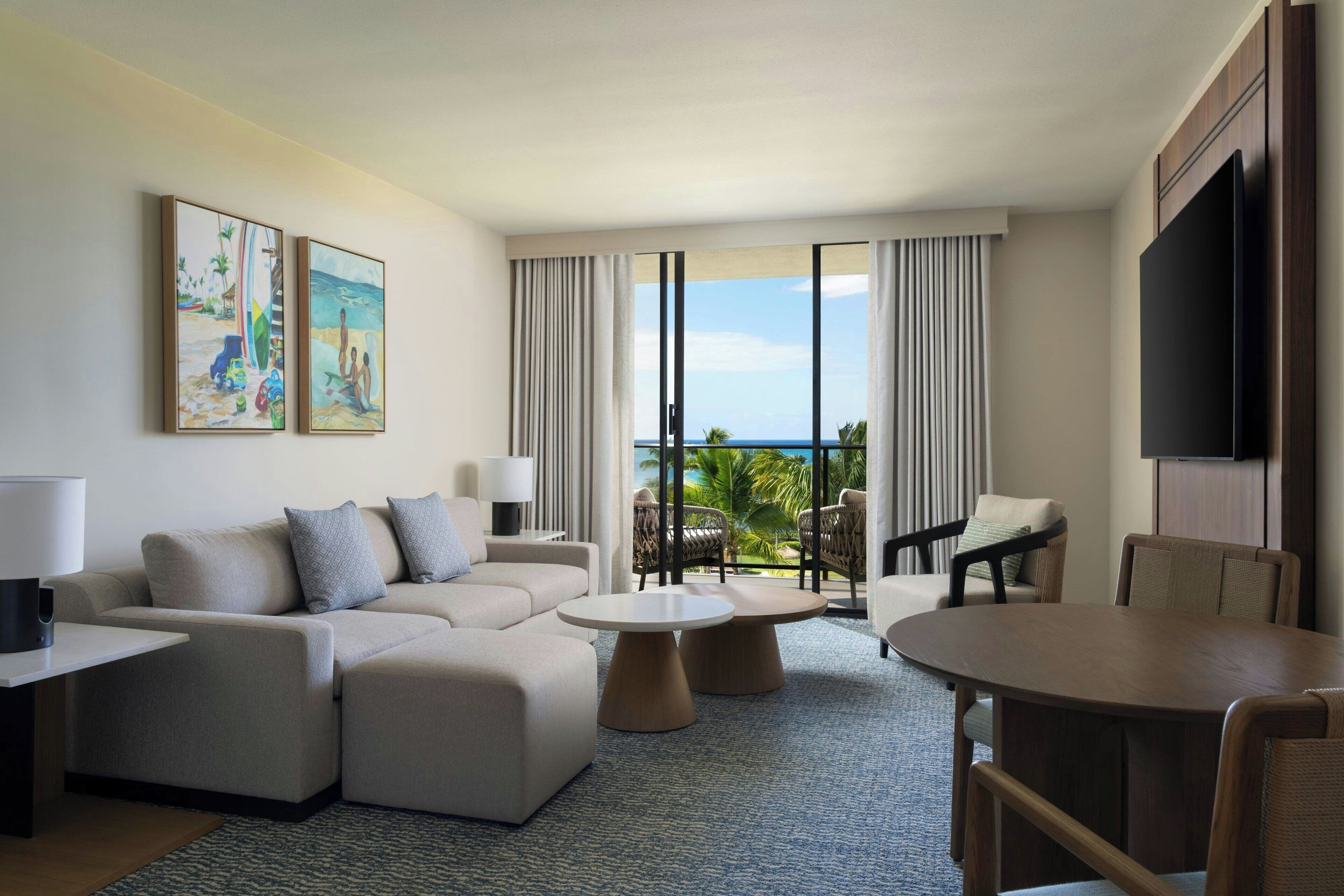 A modern hotel room with a large sofa, a dining table, and a view of the ocean.
