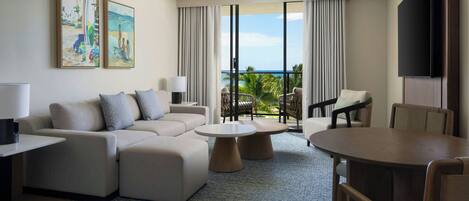 A modern hotel room with a large sofa, a dining table, and a view of the ocean.