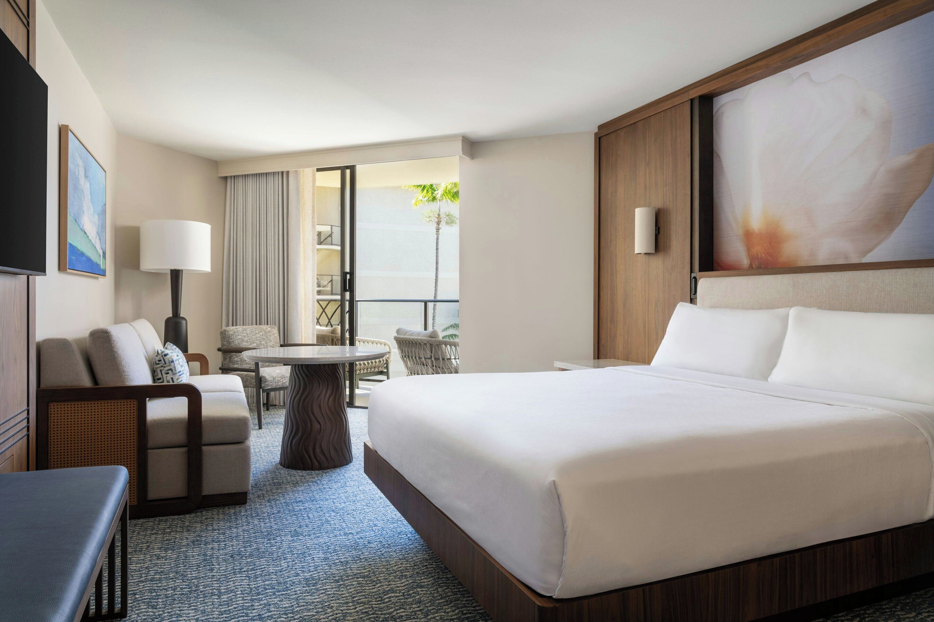 A hotel room with a large bed, a sofa, a dining table, and a balcony with a view.